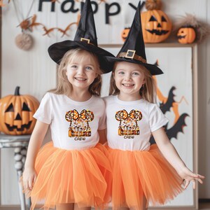 Puede incluir: Dos ni&ntilde;as peque&ntilde;as con camisetas blancas con un dise&ntilde;o de Acci&oacute;n de Gracias, tut&uacute;s naranjas y sombreros de bruja negros. Las camisetas tienen el texto "Thanksgiving Crew". Las calabazas y las decoraciones de Halloween est&aacute;n en el fondo.