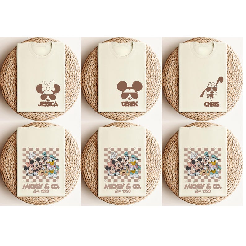 May include: Cream-colored t-shirts with brown cartoon character designs. Some shirts feature character faces with names like "Jessica", "Derek", and "Chris". Other shirts display a group of characters with the text "Mickey & Co. Est. 1928".