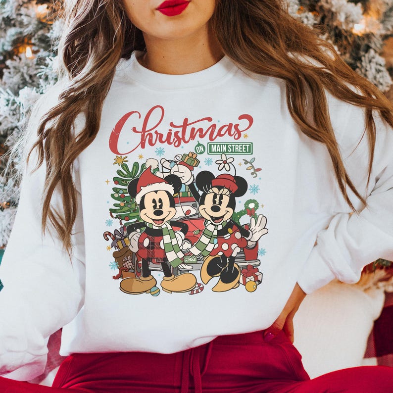 Op de afbeelding: Witte trui met een kerstontwerp met Mickey en Minnie Mouse voor een rode auto. De tekst op de trui luidt "Christmas on Main Street".