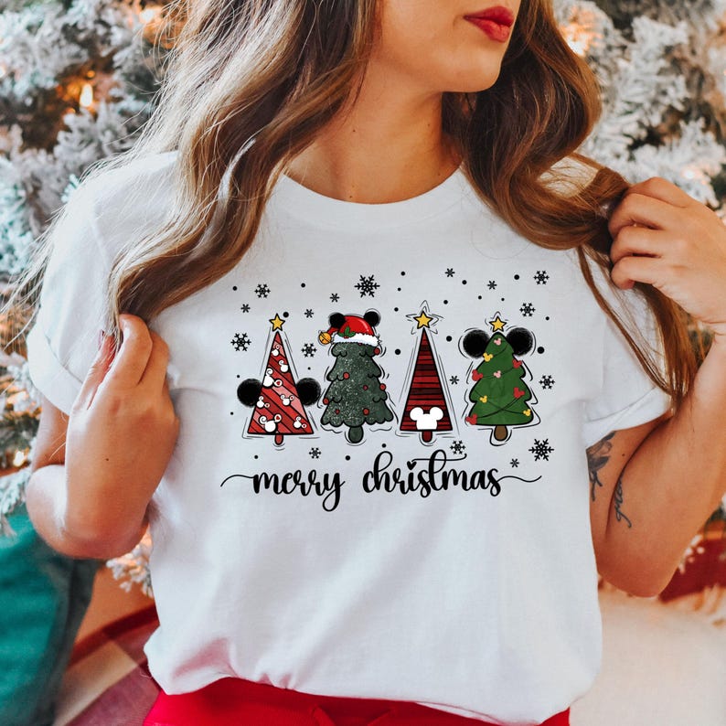 May include: White t-shirt with a Christmas design featuring four cartoon Christmas trees with Mickey Mouse ears and the text "merry christmas".