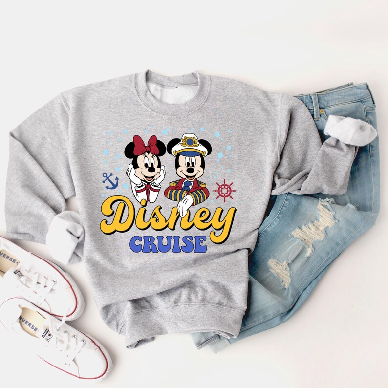 May include: Gray sweatshirt with a graphic of Mickey Mouse and Minnie Mouse dressed as a captain and a sailor. The text "Disney Cruise" is printed in yellow below the characters.
