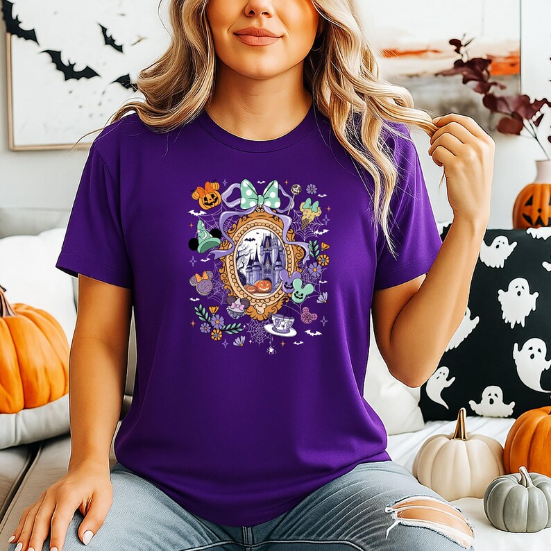 Puede incluir: Una camiseta morada con un dise&ntilde;o tem&aacute;tico de Halloween. El gr&aacute;fico incluye un castillo, calabazas y otros elementos festivos. El dise&ntilde;o est&aacute; enmarcado por un &oacute;valo dorado con un lazo verde. La camiseta es de color morado liso.