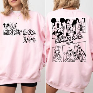 May include: Pink sweatshirt with a black graphic print of Mickey Mouse and friends. The print includes the text "Mickey & Co. Est. 1928".