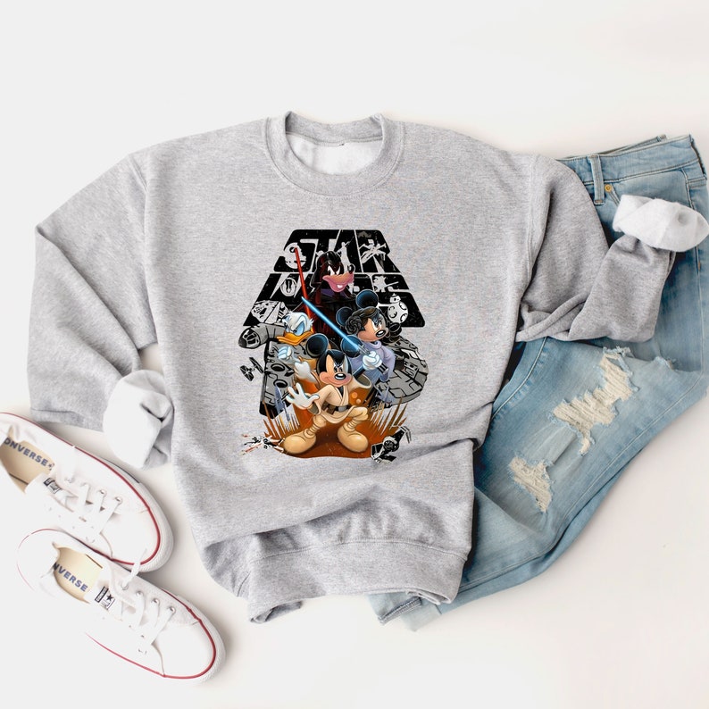 May include: A gray sweatshirt with a graphic print of Mickey Mouse, Donald Duck, and Goofy in front of the Star Wars logo. The characters are holding lightsabers and are in a fighting pose.
