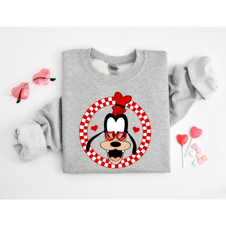 May include: Gray sweatshirt with a red and white checkered circle featuring a cartoon image of Goofy wearing heart-shaped sunglasses.
