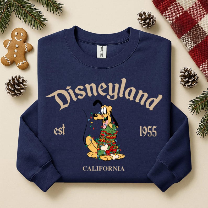 Pu&ograve; includere: Felpa blu navy con "Disneyland" in corsivo beige. Il design include Pluto con un maglione natalizio e luci, con "est 1955 CALIFORNIA" sotto. Tema festivo natalizio.