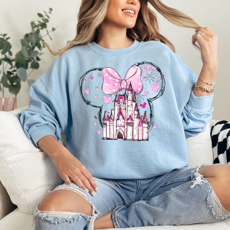 May include: Light blue sweatshirt with a pink bow and a pink castle graphic. The castle is surrounded by hearts and fireworks.