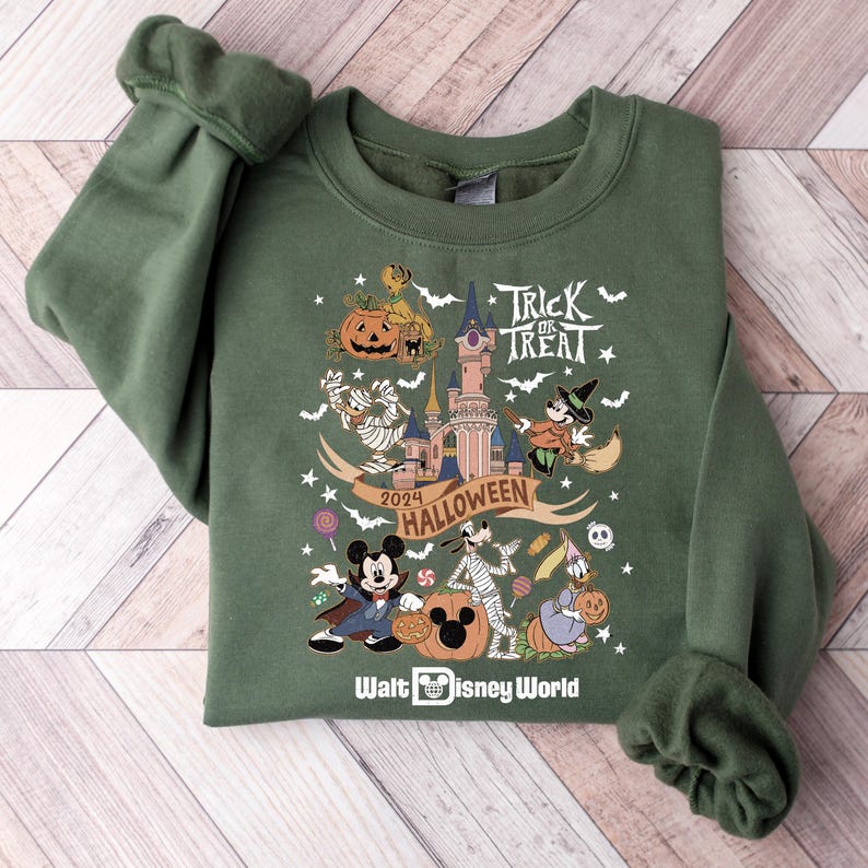 May include: A green sweatshirt with a festive Halloween design featuring Mickey Mouse, Goofy, and other Disney characters. The design includes a castle, pumpkins, candy, and the text "Trick or Treat" and "2024 Halloween". The bottom of the sweatshirt has the text "Walt Disney World".