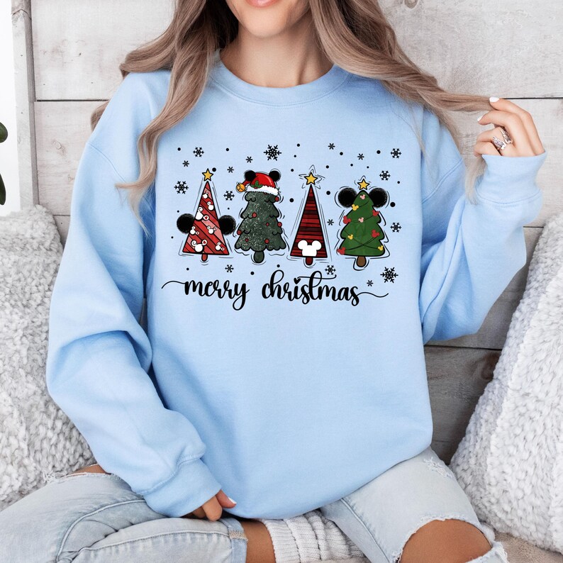 May include: Light blue sweatshirt with a Christmas design featuring four cartoon Christmas trees with Mickey Mouse ears and the text "merry christmas".