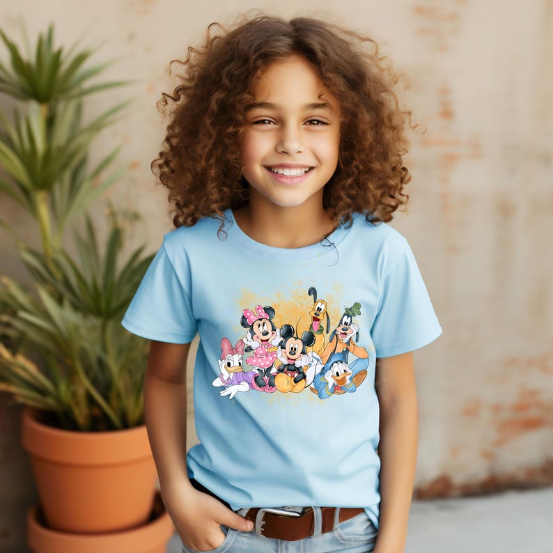 Puede incluir: Una camiseta azul claro con un estampado gr&aacute;fico colorido de Mickey Mouse, Minnie Mouse, Donald Duck, Goofy y Pluto. Los personajes sonr&iacute;en y est&aacute;n de pie juntos.