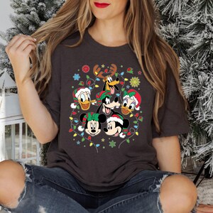 May include: A dark gray t-shirt with a Christmas-themed design featuring Mickey Mouse, Minnie Mouse, Donald Duck, Goofy, and Pluto. The characters are surrounded by colorful Christmas lights and snowflakes.