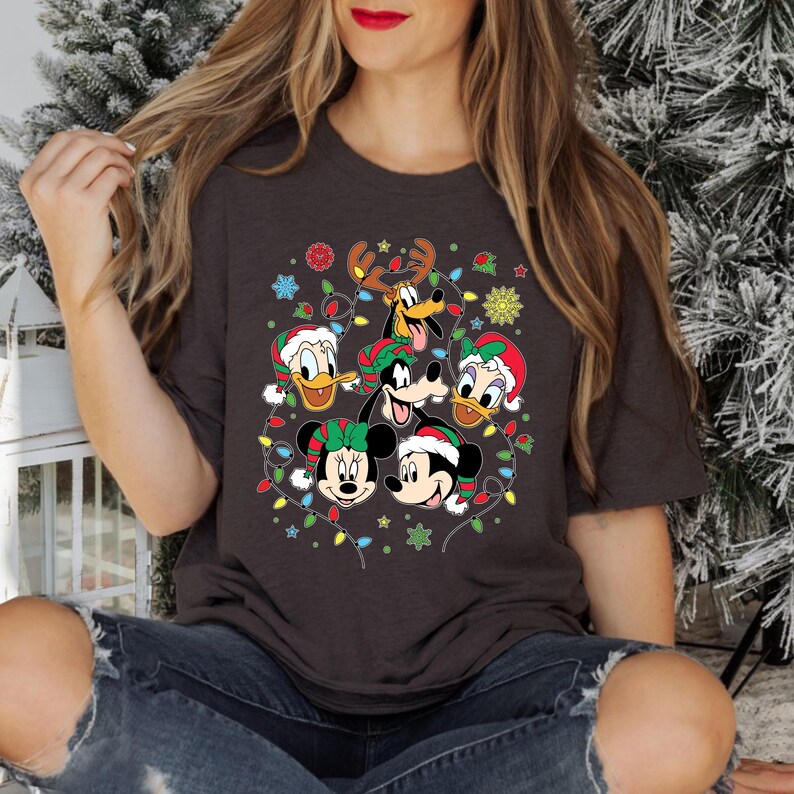 May include: A dark gray t-shirt with a Christmas-themed design featuring Mickey Mouse, Minnie Mouse, Donald Duck, Goofy, and Pluto. The characters are surrounded by colorful Christmas lights and snowflakes.