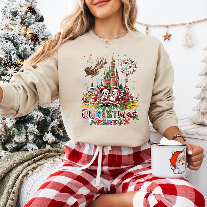 May include: Beige sweatshirt featuring a colorful graphic of Disney characters in Christmas attire in front of a castle. The text "Merry Christmas Party" is below the graphic. The person is wearing red and white plaid pajama pants.