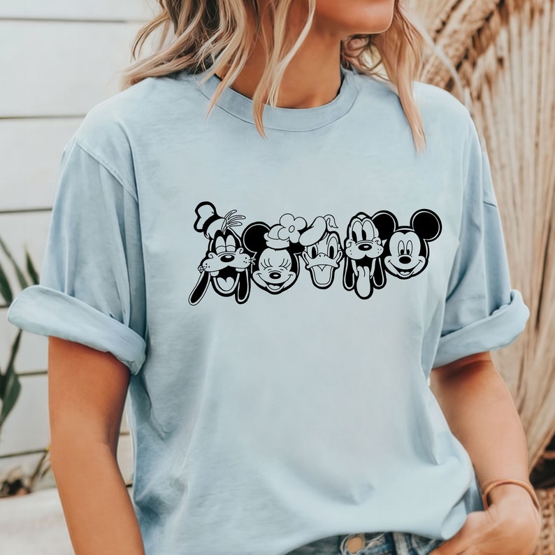 K&ouml;nnte beinhalten: Ein hellblaues T-Shirt mit einer schwarz-wei&szlig;en Grafik von Mickey Mouse, Minnie Mouse, Donald Duck, Goofy und Pluto. Die Figuren sind horizontal angeordnet und l&auml;cheln.