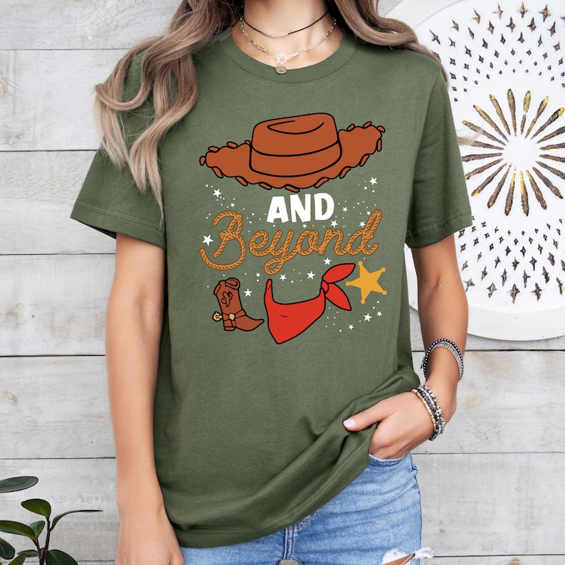 Peut inclure: T-shirt &agrave; manches courtes de couleur verte avec une image de dessin anim&eacute; d'un chapeau de cowboy, un bandana rouge, une botte de cowboy et une &eacute;toile. Le texte "AND BEYOND" est &eacute;crit dans une police de caract&egrave;res en forme de corde.