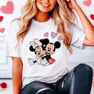May include: White t-shirt with a graphic of Mickey Mouse and Minnie Mouse hugging, surrounded by pink hearts.