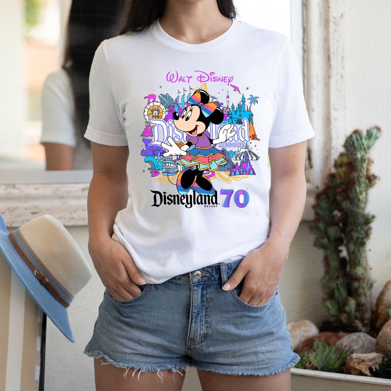 May include: White t-shirt with a colorful graphic of Minnie Mouse in front of Disneyland park icons. The text "Walt Disney" and "Disneyland Resort 70" is printed on the shirt.