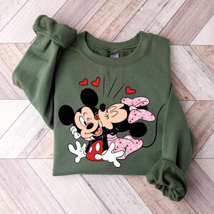 May include: Green sweatshirt featuring a printed design of Mickey Mouse and Minnie Mouse kissing. The print includes red hearts and the text "Oh Boy".