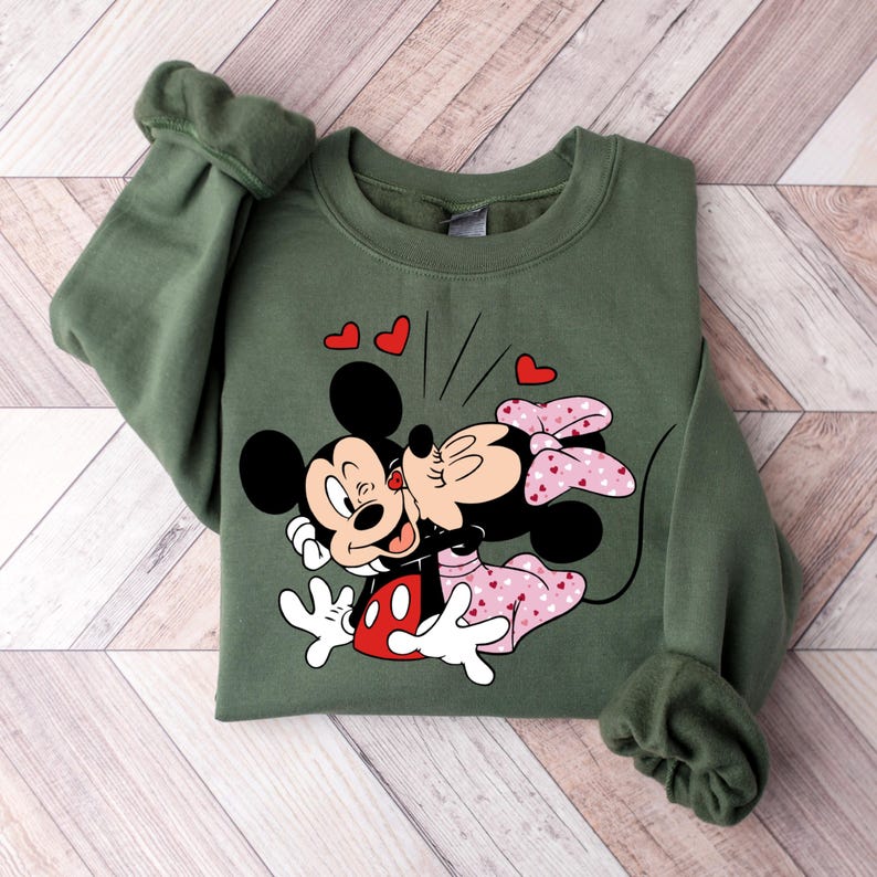 May include: Green sweatshirt featuring a printed design of Mickey Mouse and Minnie Mouse kissing. The print includes red hearts and the text "Oh Boy".