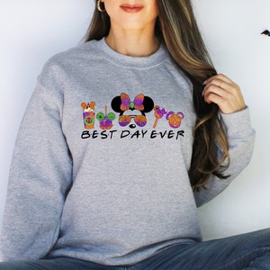 May include: Gray sweatshirt with a Halloween-themed graphic featuring Mickey Mouse, Minnie Mouse, and other Disney characters. The text "BEST DAY EVER" is printed below the graphic.