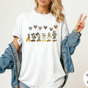 K&ouml;nnte beinhalten: Wei&szlig;es T-Shirt mit Zeichentrickfiguren, die Luftballons mit Tiermotiven halten. Die Figuren sind Pluto, Micky Maus, Minnie Maus, Donald Duck und Goofy. Das Shirt hat die Worte "Comfort Colors White" unten rechts.