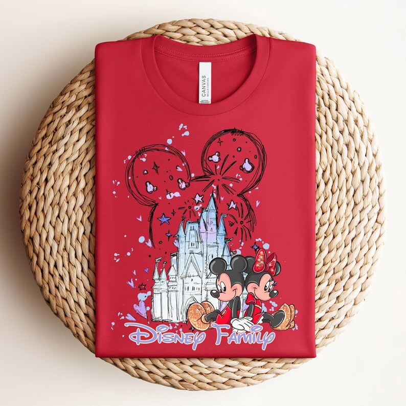 May include: Red t-shirt with a graphic of Mickey and Minnie Mouse in front of a castle, with the words "Disney Family" in purple script. The design includes fireworks and Mickey Mouse ears.