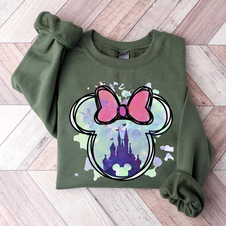 May include: Green sweatshirt with a watercolor-style Mickey Mouse head design. The design features a pink bow and a silhouette of Cinderella's castle inside the ears.