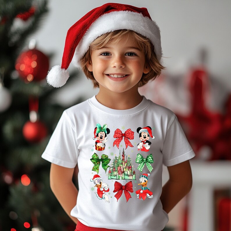 May include: A white t-shirt with a Christmas theme featuring Mickey Mouse, Minnie Mouse, Donald Duck, and a Christmas castle. The shirt has red and green bows and a red Santa hat.
