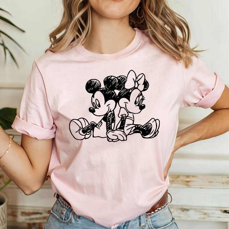 May include: A pink t-shirt with a black and white graphic of Mickey Mouse and Minnie Mouse holding hands.
