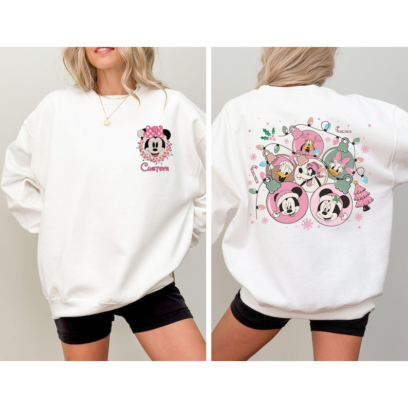 May include: White sweatshirt featuring a Minnie Mouse graphic with a pink bow and the word "Custom" on the front. The back of the sweatshirt displays Christmas ornaments with Disney characters. Festive and seasonal apparel.