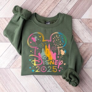 May include: A green sweatshirt with a rainbow-colored Mickey Mouse silhouette and the text "DISNEY 2025" on the front.