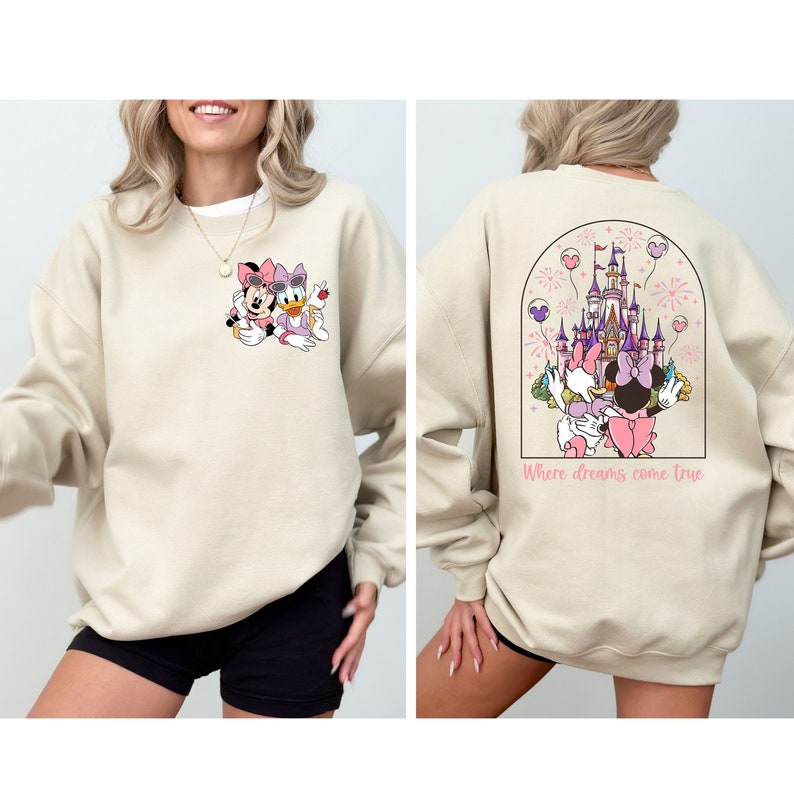 Pu&ograve; includere: Una felpa beige con un'immagine di cartone animato di Topolino e Paperina sul davanti e un'immagine di cartone animato del castello di Cenerentola con Topolino e Paperina sul retro. Il testo "Where dreams come true" &egrave; stampato sotto l'immagine sul retro.