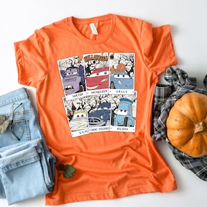 May include: Orange t-shirt with a Halloween themed graphic featuring the Cars characters Mater, McQueen, Sally, Luigi, Doc Hudson, and Guido. The graphic is in a vintage style with a distressed look.
