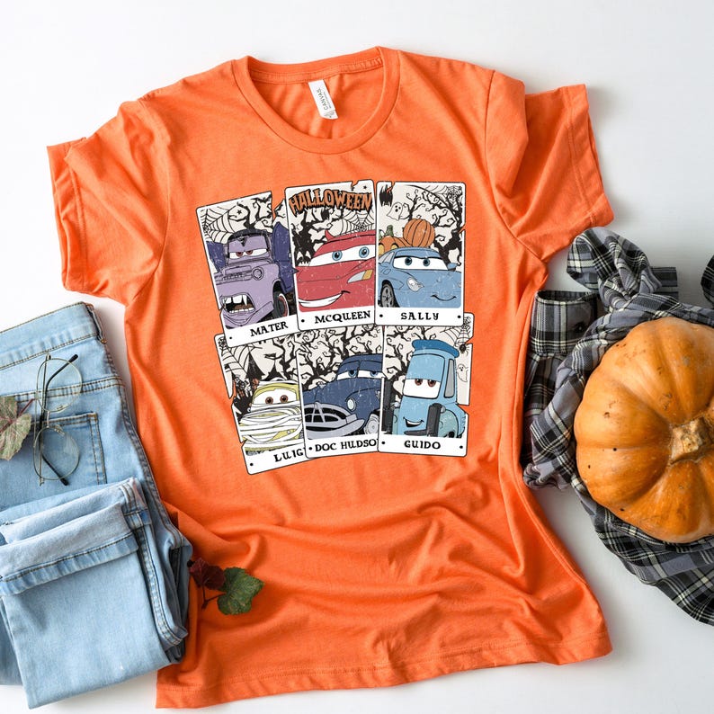 May include: Orange t-shirt with a Halloween themed graphic featuring the Cars characters Mater, McQueen, Sally, Luigi, Doc Hudson, and Guido. The graphic is in a vintage style with a distressed look.