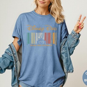 May include: Blue jean-coloured t-shirt with the text "Disney Dad" in gold. The shirt features a barcode design with a castle silhouette and Mickey Mouse ears. The shirt is a comfort colour.