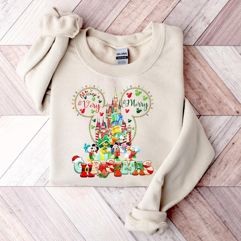 May include: A beige sweatshirt with a Christmas-themed design featuring Mickey Mouse's ears, a depiction of Cinderella's Castle, and the text "Mickey's Very Merry Christmas".