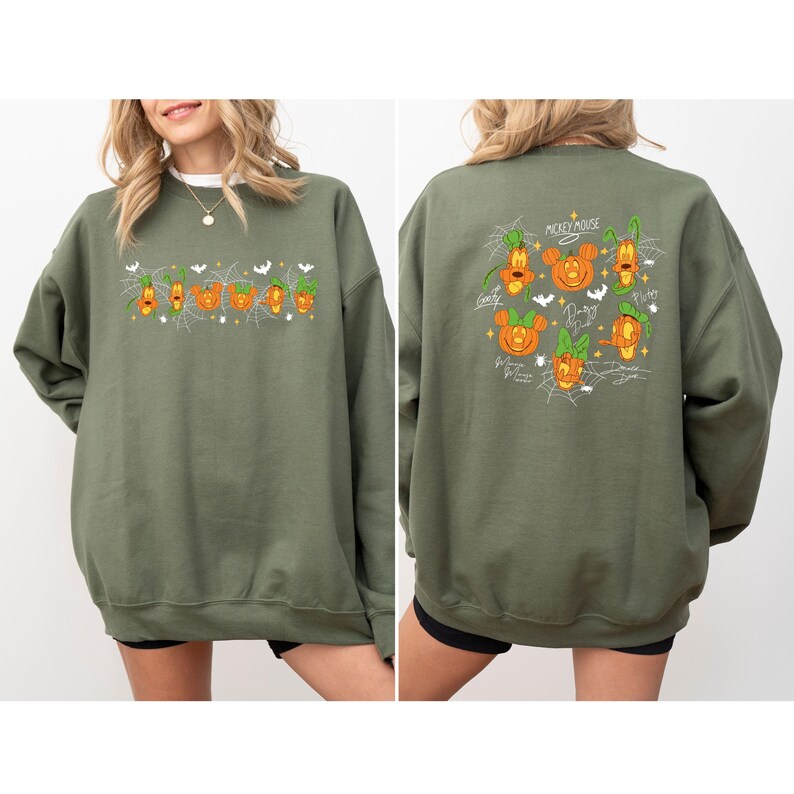 May include: Olive green sweatshirt featuring Halloween-themed Mickey Mouse and friends. The front displays the word "Boo" with pumpkin and spiderweb graphics. The back showcases character portraits in pumpkin designs, with signatures and "Mickey Mouse" text.