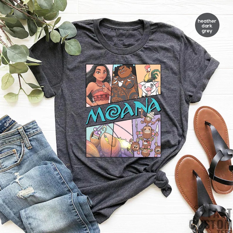 May include: Heather dark grey t-shirt with a cartoon image of Moana, Maui, Pua, and the Kakamora. The shirt has the word "Moana" printed in blue on the front.