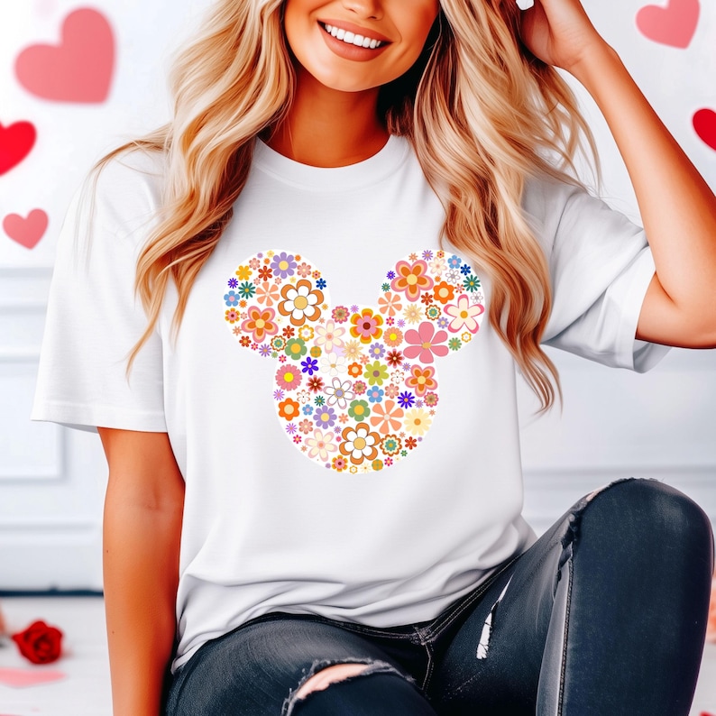 May include: White t-shirt featuring a floral Mickey Mouse design. The design is composed of various colorful flowers in shades of orange, pink, yellow, and blue. The shirt is a classic crew neck style.