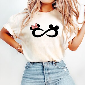 May include: A white t-shirt with a black infinity symbol design featuring a red and white polka dot bow on one side and a black Mickey Mouse ear on the other side.