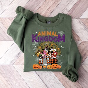 May include: An olive green sweatshirt with the words "ANIMAL KINGDOM" in purple and white. The graphic features Disney characters in a Halloween design with pumpkins and spiderwebs.