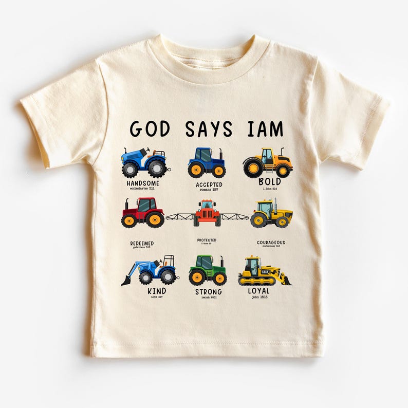 May include: A beige t-shirt with the text "GOD SAYS IAM" printed on the front. The text is surrounded by illustrations of tractors with different colors and designs. Each tractor is labeled with a positive word, such as "handsome", "accepted", "bold", "redeemed", "protected", "courageous", "kind", "strong", and "loyal".