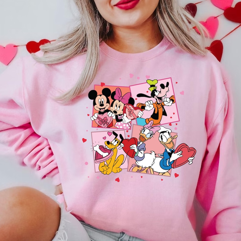 May include: Pink sweatshirt with a graphic print of Mickey Mouse, Minnie Mouse, Goofy, Pluto, and Donald Duck holding Valentine's Day hearts.