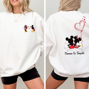 May include: White sweatshirt with a Mickey Mouse and Minnie Mouse graphic on the front and a Mickey Mouse and Minnie Mouse graphic with a heart balloon and the text "Thomas & Sophia" on the back.