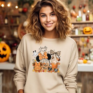 May include: Beige sweatshirt with a Halloween-themed graphic. The graphic includes a Minnie Mouse design with a pumpkin, ghost, spiderwebs, and the text "Literally just a girl". The design also features a bow, sunglasses, and fall leaves.