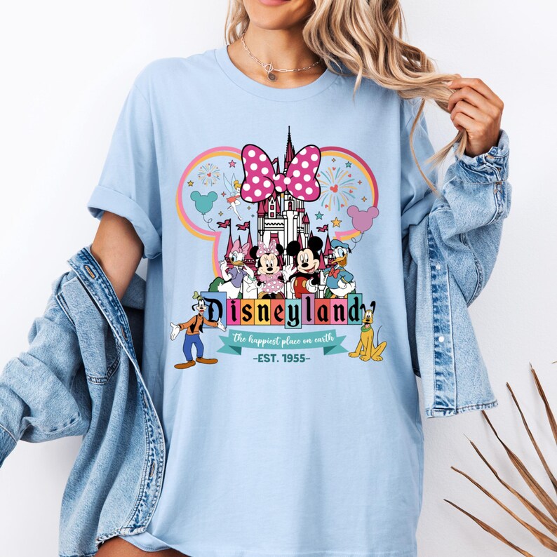 May include: Light blue t-shirt with a colorful graphic of Mickey Mouse and friends in front of the Disneyland castle. The text "Disneyland" is written in a colorful font with the tagline "The happiest place on earth -EST. 1955-."