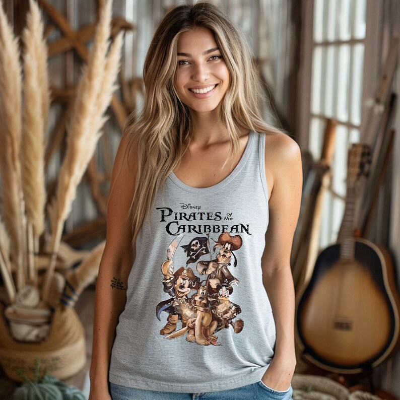 Pode incluir: Um top de al&ccedil;as cinza com uma estampa gr&aacute;fica de Mickey Mouse, Pateta e Pluto vestidos de piratas. O texto "Disney Pirates of the Caribbean" est&aacute; impresso acima dos personagens.