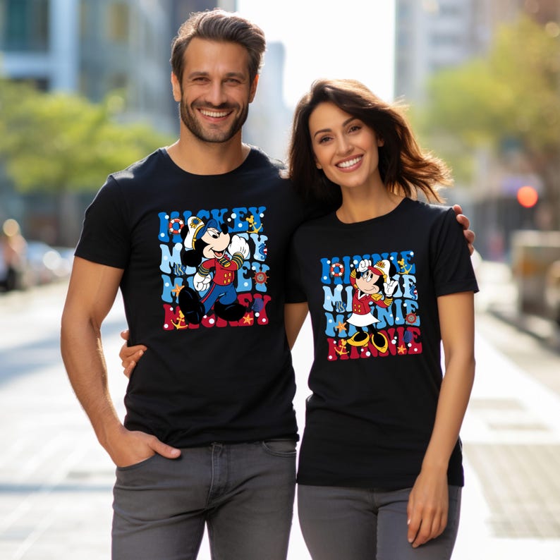 May include: A couple wearing black t-shirts with a nautical themed Mickey Mouse and Minnie Mouse graphic. The shirts feature the text "Mickey Mouse" and "Minnie Mouse" in a colorful, retro style.