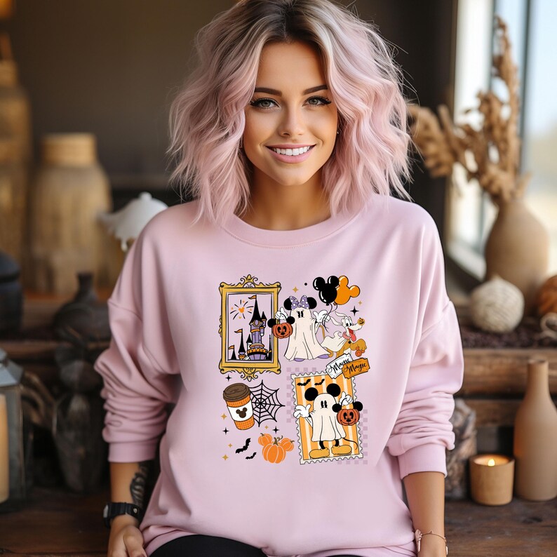 Puede incluir: Sudadera rosa claro con un dise&ntilde;o de Halloween. El gr&aacute;fico incluye un castillo enmarcado, un fantasma, Mickey Mouse, calabazas y las palabras "Minnie Magic". La sudadera tiene mangas largas y cuello redondo.