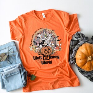 Puede incluir: Camiseta naranja con un dise&ntilde;o de Halloween con personajes de Disney, una calabaza tallada y el texto "Walt Disney World". El dise&ntilde;o incluye murci&eacute;lagos, un castillo embrujado y la frase "the most magical place on earth".